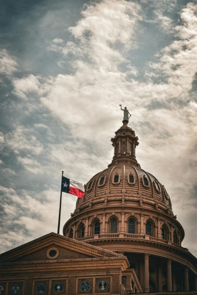 Close-up of the Texas State Capitol dome with Texas flag against a cloudy sky in Austin.